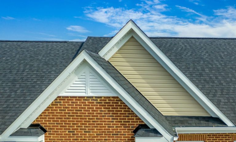 Double gable with beige horizontal vinyl lap and red brick facade siding, with triangle shape white attic vent on a pitched roof attic, Edina